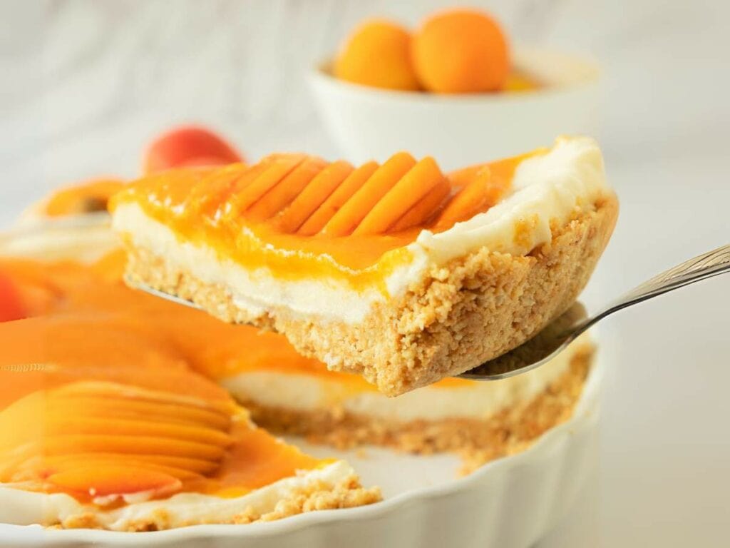 A close-up of a slice of creamy apricot cheesecake with a crumbly crust.