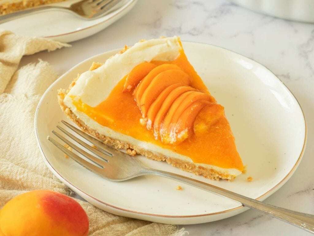 A slice of apricot cheesecake tart on a white plate with a fork.