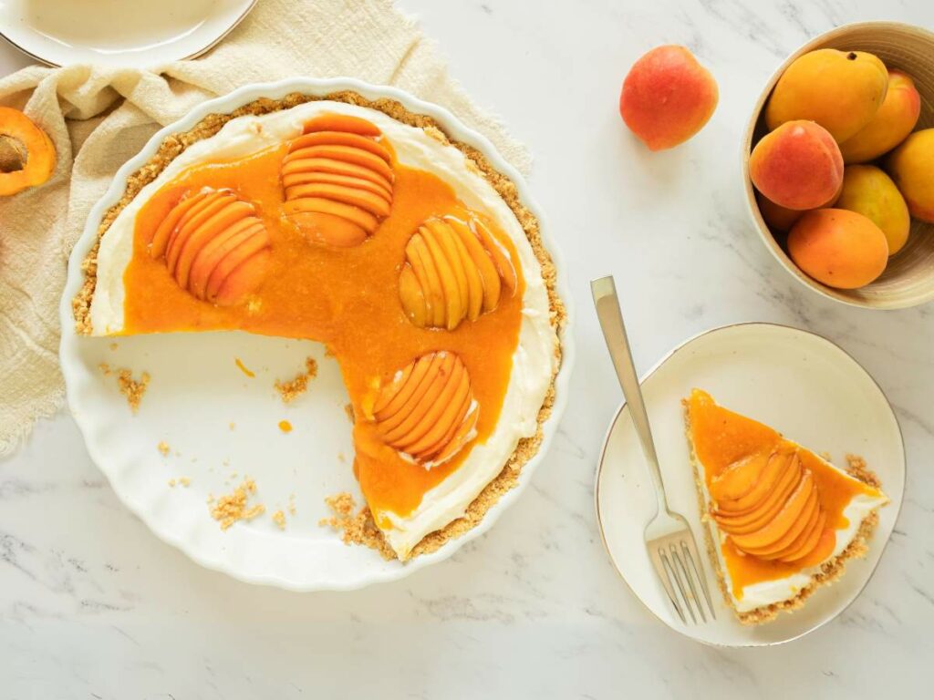 A sliced apricot cheesecake with cream filling on a white plate, accompanied by a fork.