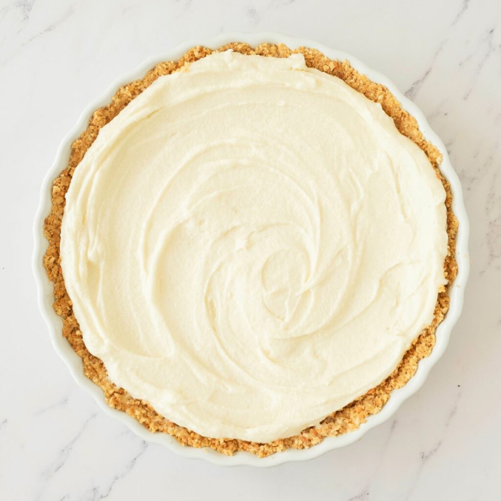 A pie with a crumbly crust and a smooth, creamy white filling sits on a white marble surface.