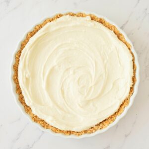 A pie with a crumbly crust and a smooth, creamy white filling sits on a white marble surface.