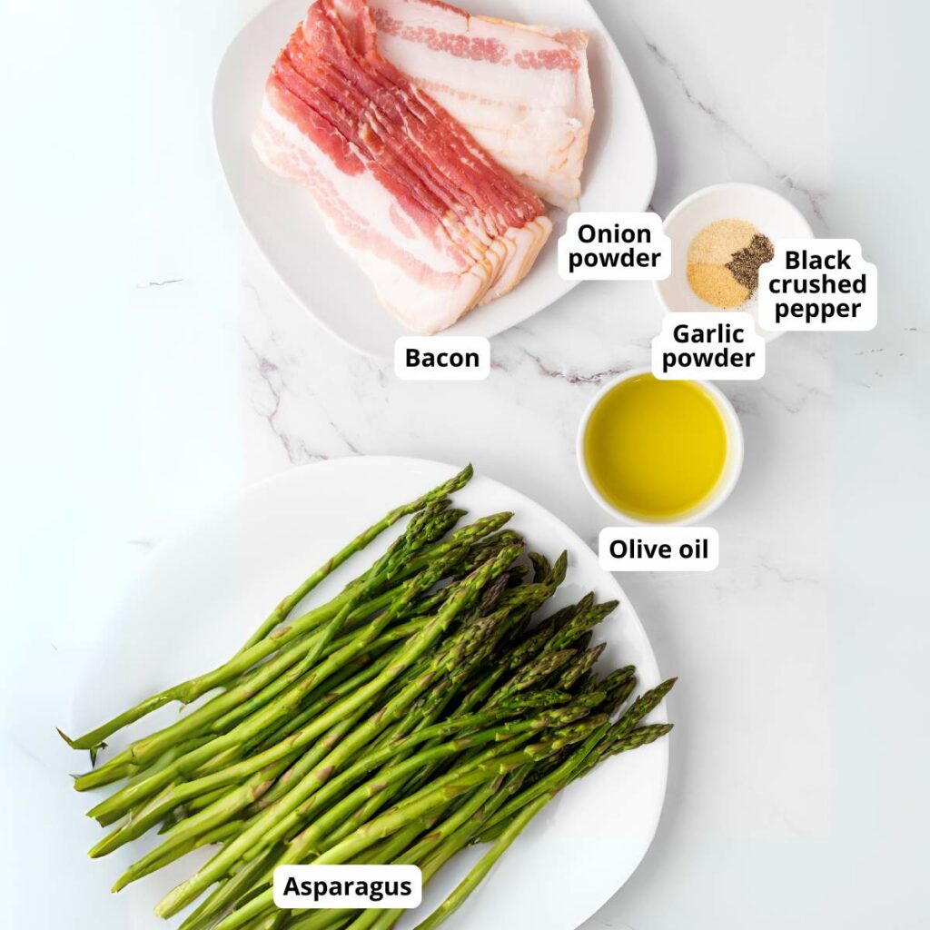 Two plates on a white surface, one with raw bacon, onion powder, garlic powder, black crushed pepper, and olive oil; the other with fresh asparagus spears.