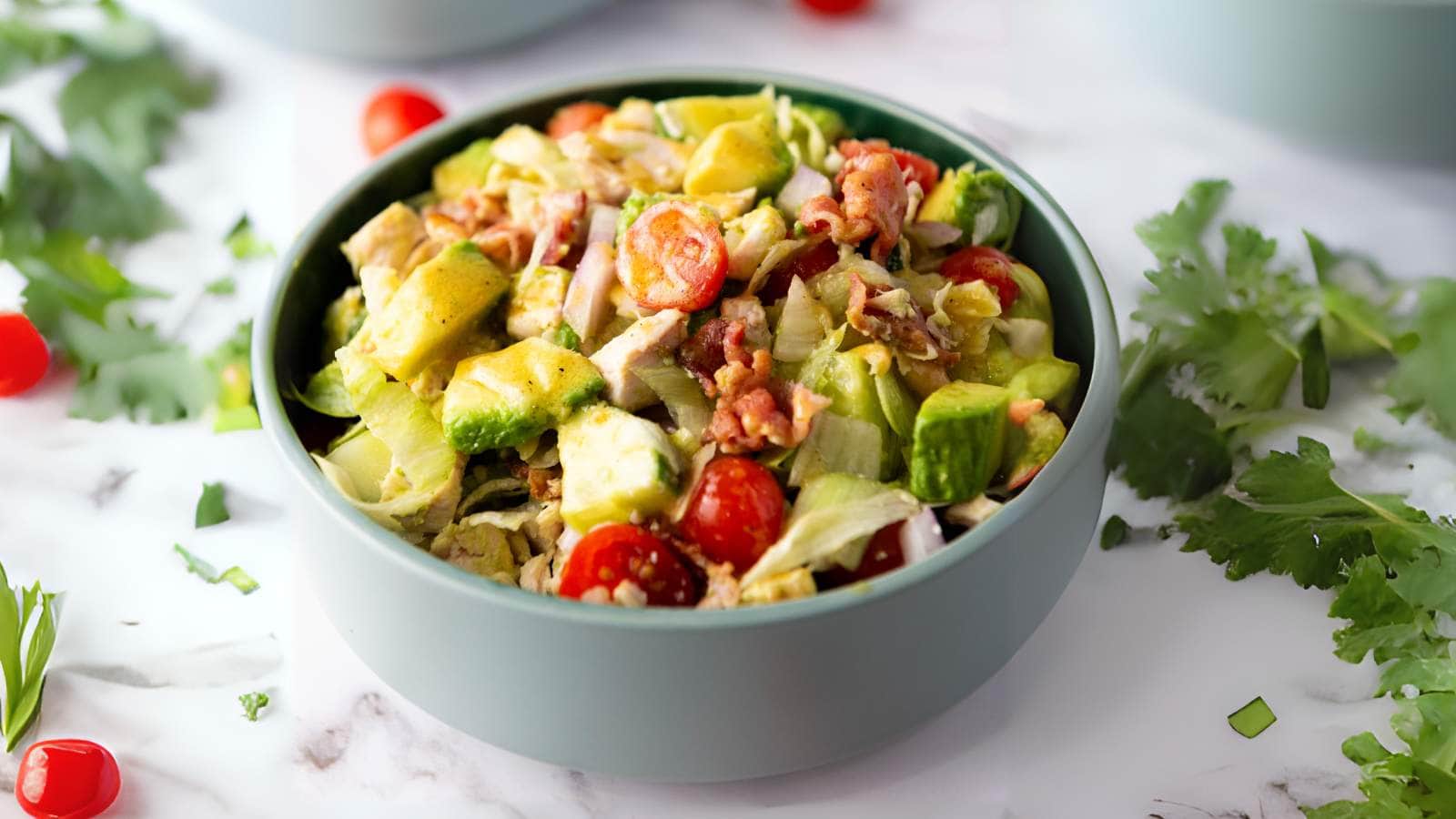 A bowl filled with chopped chicken salad, and dressing sits on a white surface.