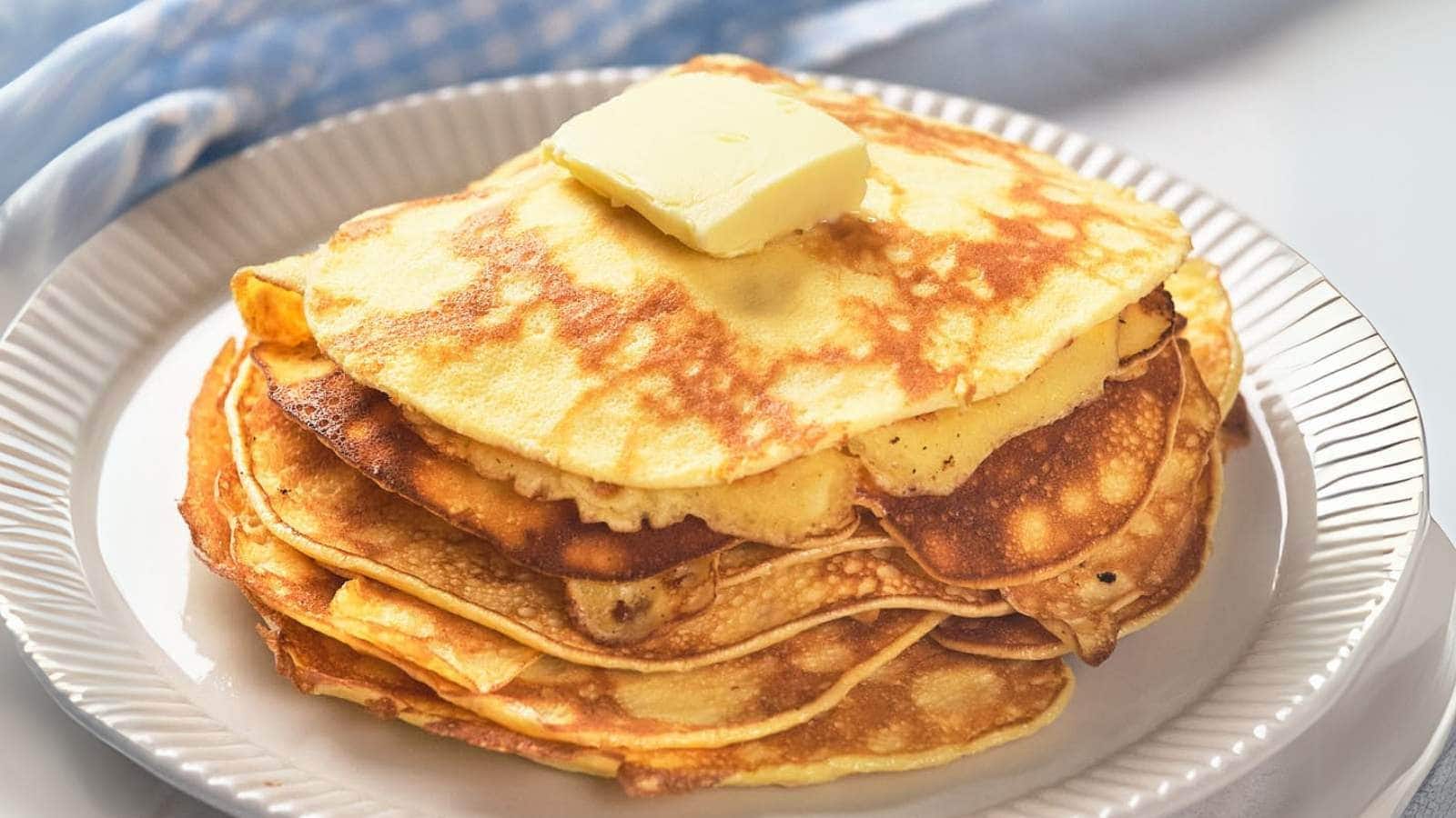 A stack of golden pancakes topped with a square of butter on a white plate.