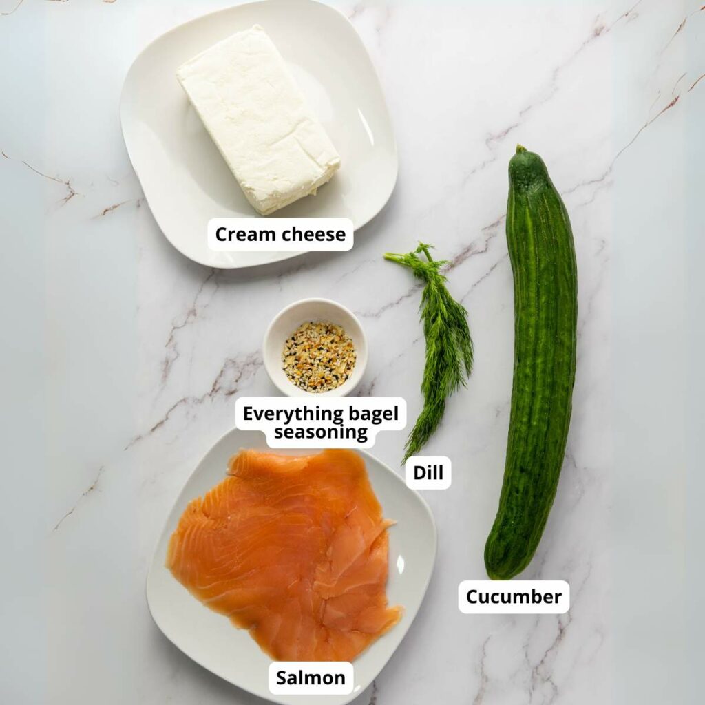 Plates with cream cheese and smoked salmon, a bowl of everything bagel seasoning, a bunch of dill, and a whole cucumber.