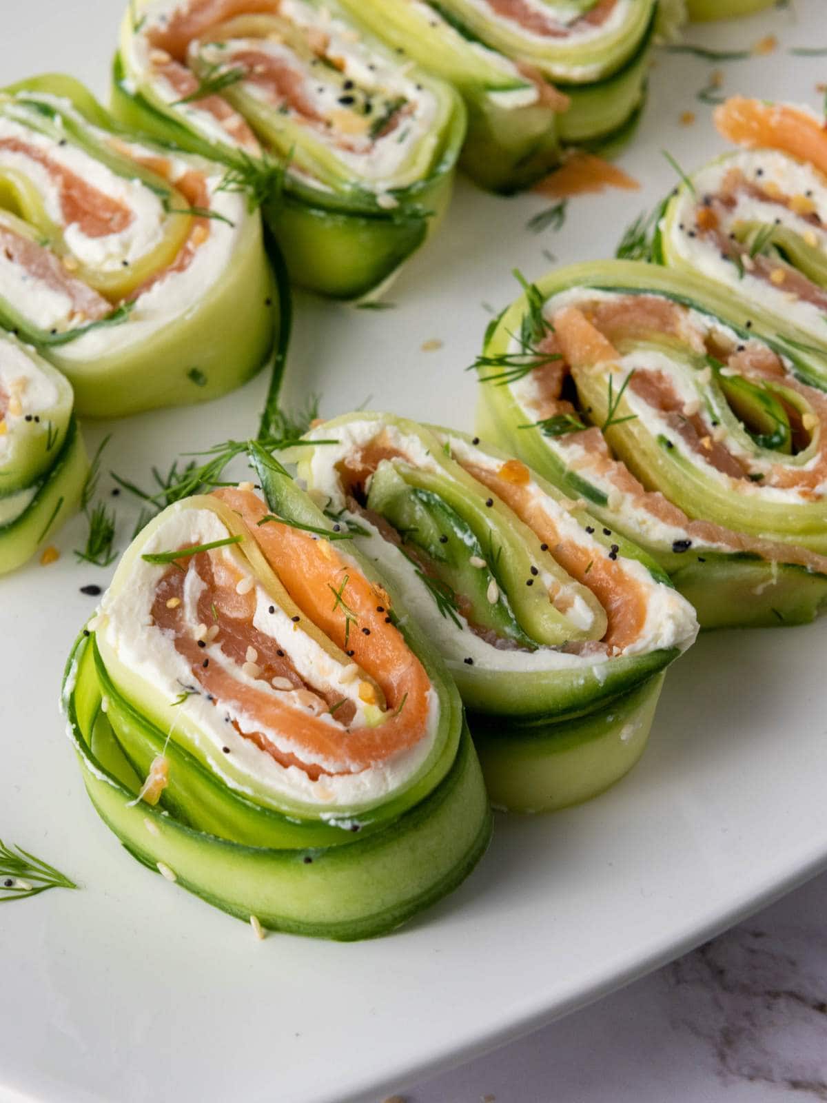 Rolled cucumber slices filled with cream cheese and smoked salmon, garnished with fresh dill.