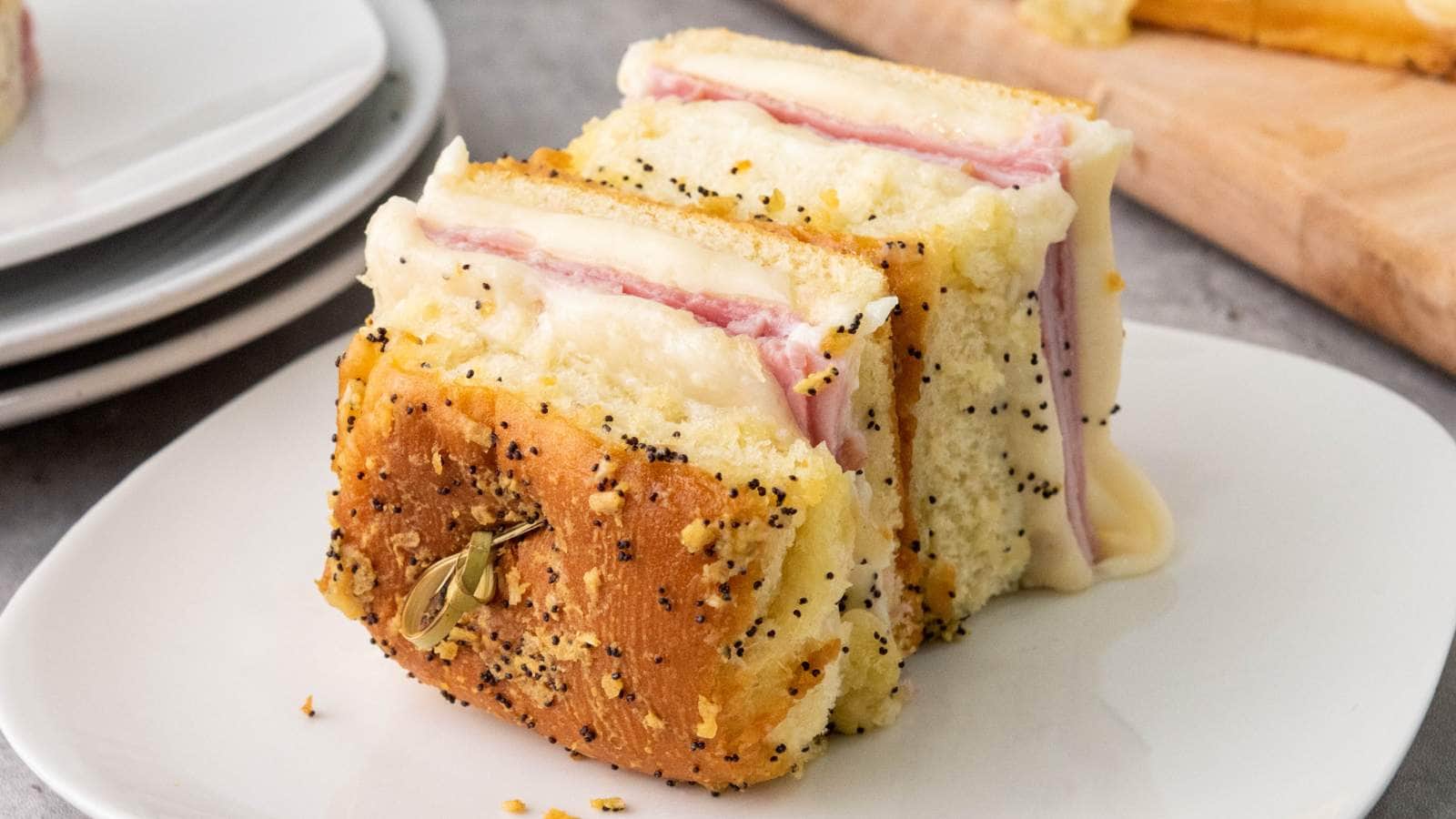 Two slices of baked ham and cheese sliders on hawaiian rolls with poppy seeds and seasonings.