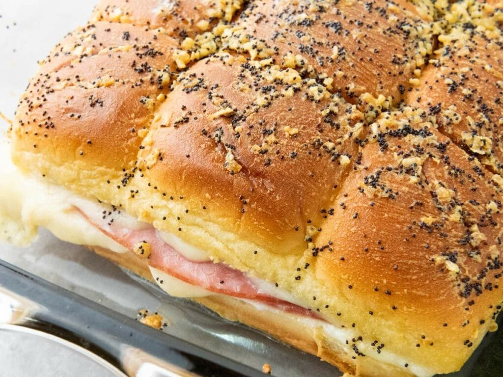A close-up of baked ham and cheese sliders on hawaiian rolls on soft rolls.