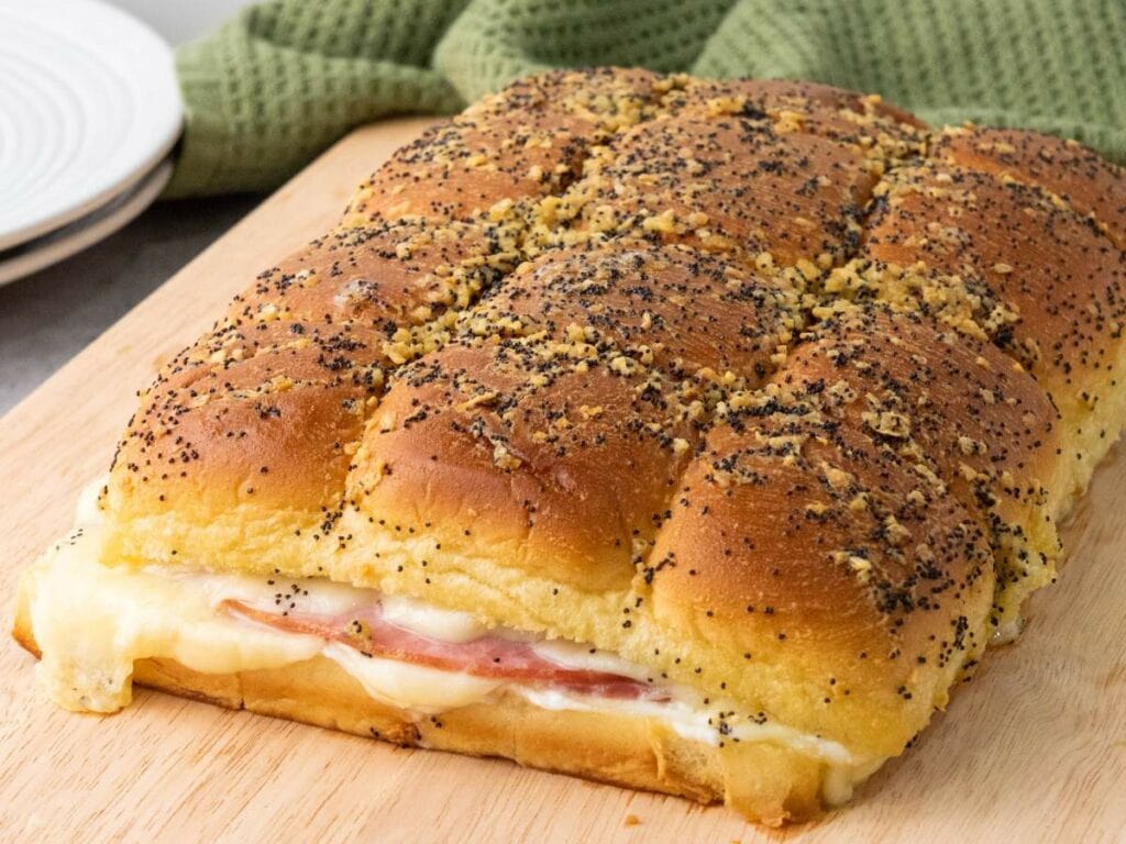 Ham and cheese sliders on hawaiian rolls with poppy seeds and seasoning on top.