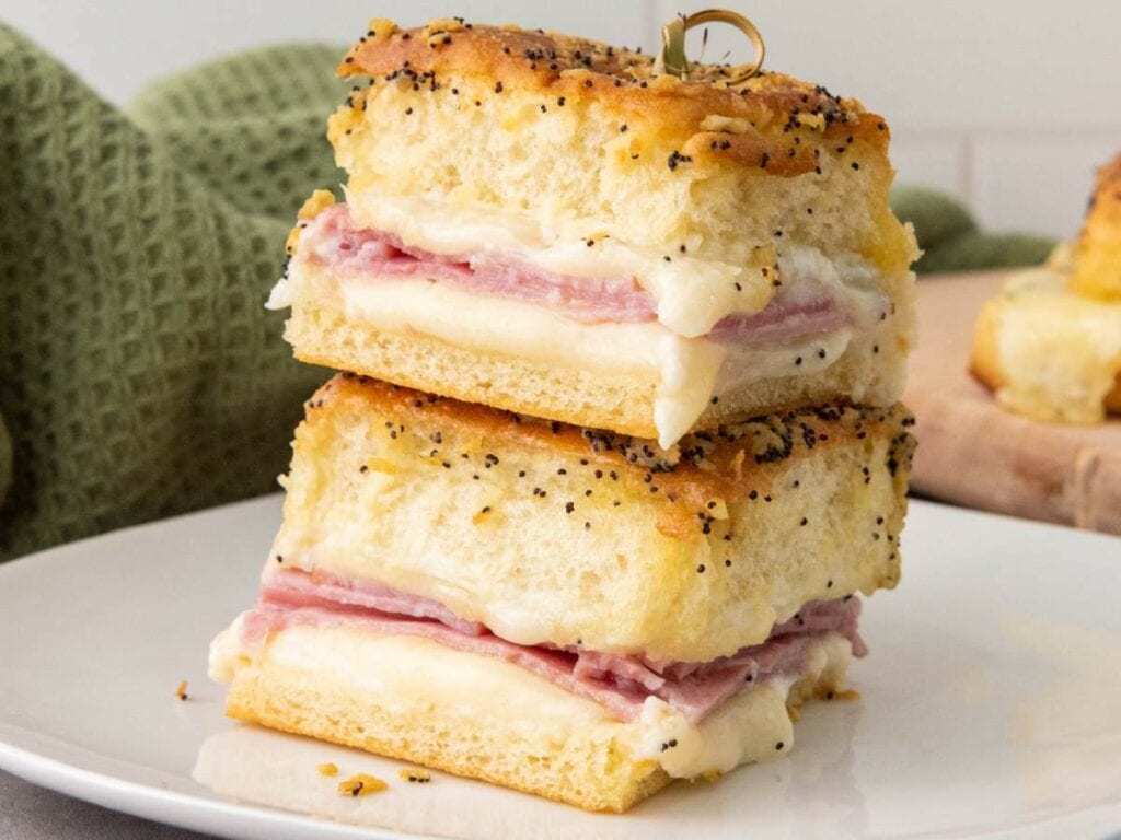 Two stacked ham and cheese sliders on hawaiian rolls on a white plate.