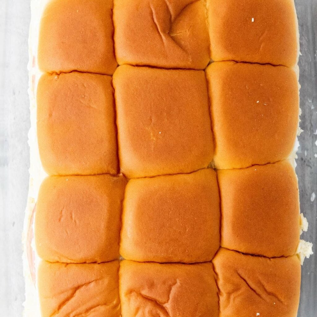 Nine evenly arranged sandwich slider buns viewed from above on a light surface.