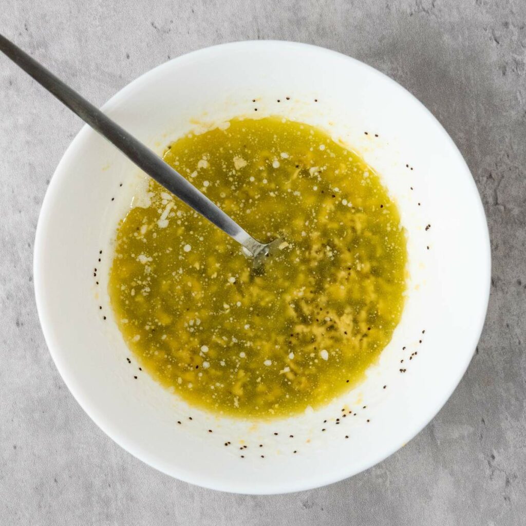 A white bowl with a metal spoon contains a greenish-yellow liquid mixture.