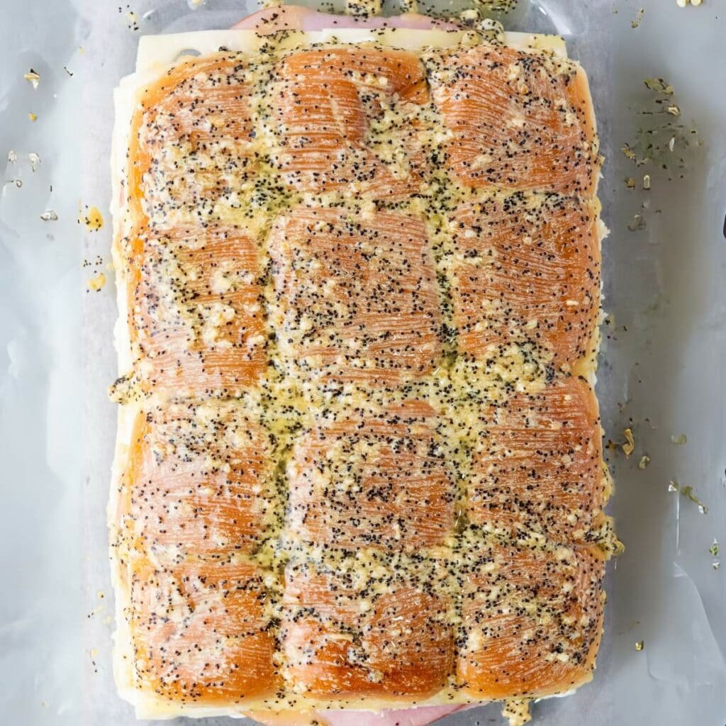 A tray of sliced sandwich rolls filled with layers of ham and cheese.