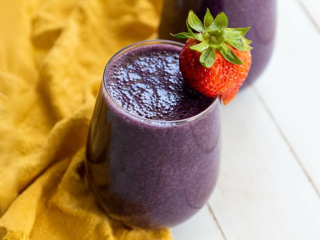 A glass of mixed berry smoothie topped with a whole strawberry, placed on a white surface.