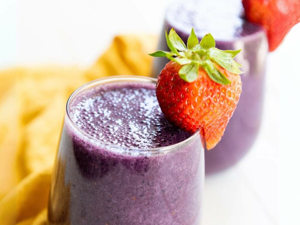 A glass of mixed berry smoothie garnished with a whole strawberry, with another glass in the background.
