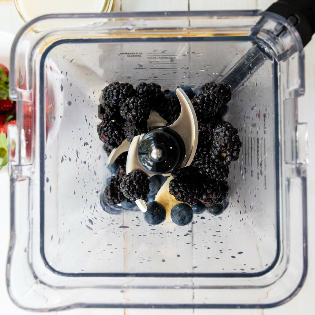 Overhead view of a blender containing blackberries, blueberries, and banana pieces, ready to be blended.