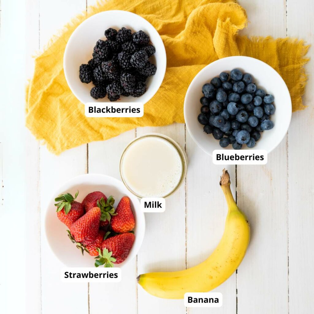 Labeled ingredients for mixed berry smoothie on a white wooden surface.