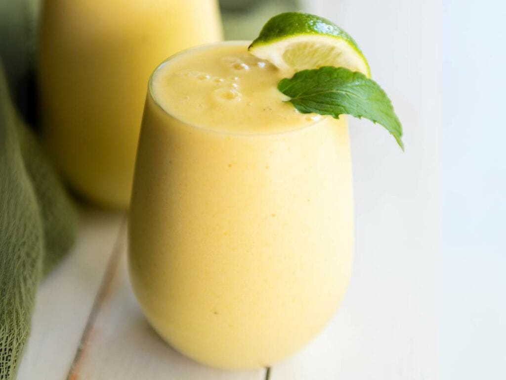 A glass of yellowpineapple and banana leaf, placed on a white surface.