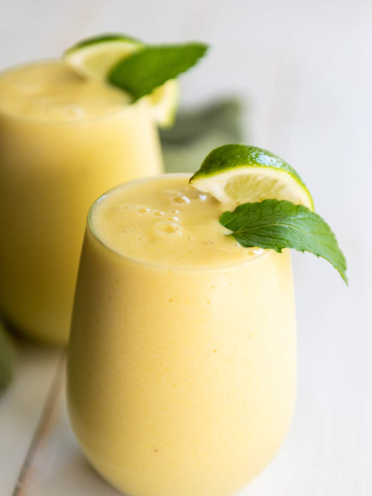 A glass of pineapple and banana smoothie garnished with a lime wedge and mint leaf.