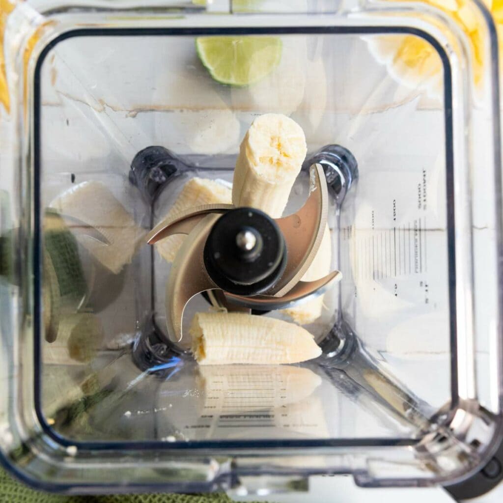A peeled banana is cut in half and placed inside a blender, viewed from above.
