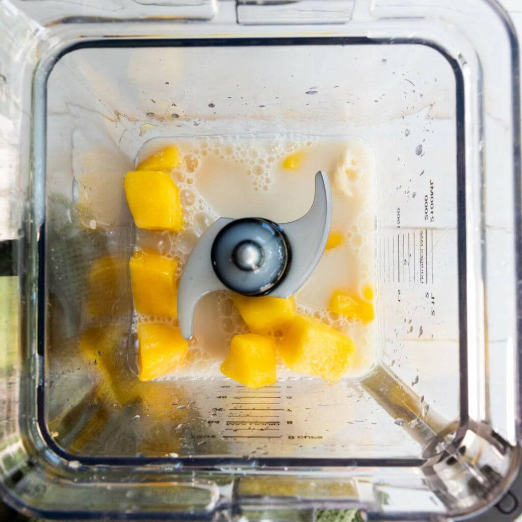 Cubed mango pieces and milk in a blender jar viewed from above, ready to be blended.