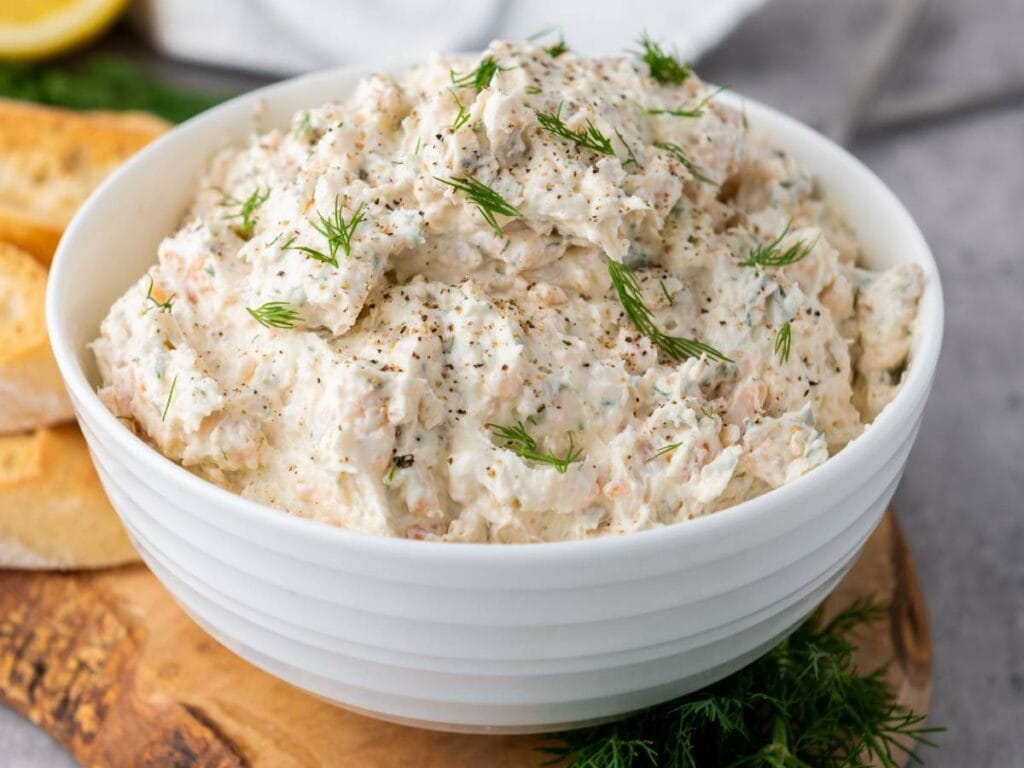 A white bowl filled with smoked salmon spread garnished with dill and black pepper.