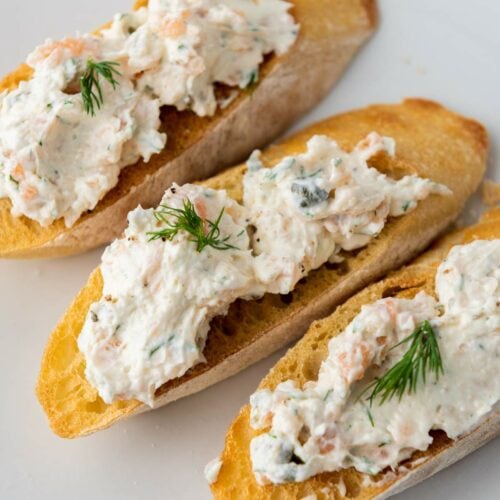 Three toasted baguette slices topped with a smoked salmon spread containing herbs.