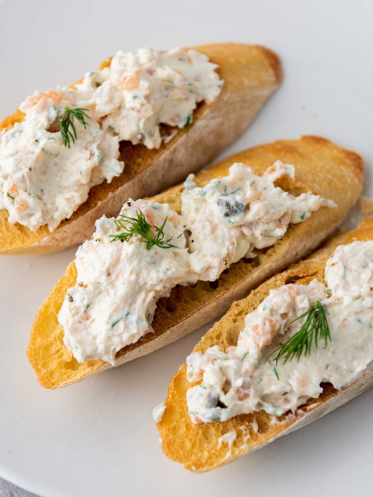 Three toasted baguette slices topped with a smoked salmon spread containing herbs.