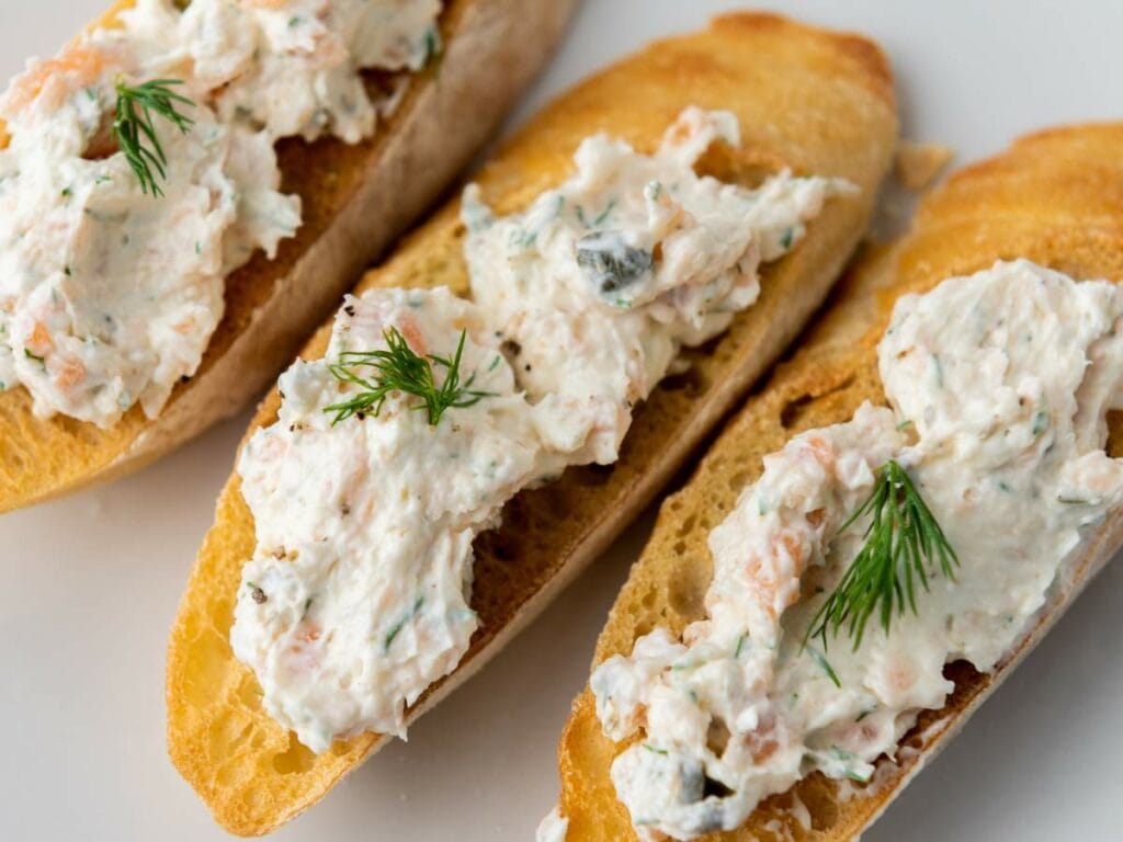 Three toasted baguette slices topped with smoked salmon spread containing herbs.