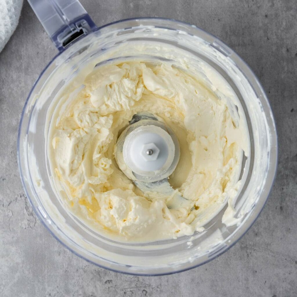 A food processor containing a creamy, whipped mixture sits on a gray countertop.