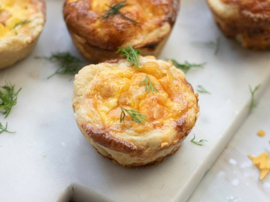Smoked salmon tartlets topped with fresh dill on a marble surface.