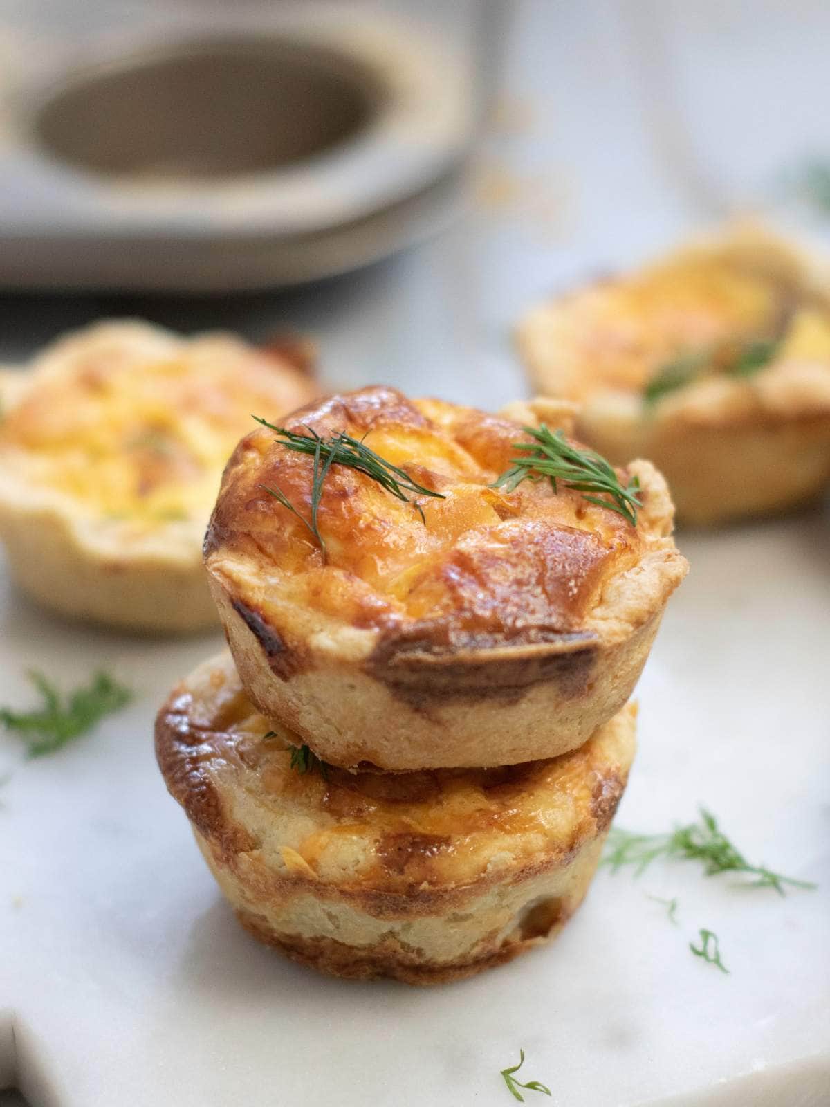 Two smoked salmon tartlets are stacked on a white surface, garnished with fresh dill.