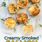 Seven smoked salmon tartlets garnished with dill are arranged on a white marble surface, with text reading, "Creamy Smoked Salmon Tartlets.