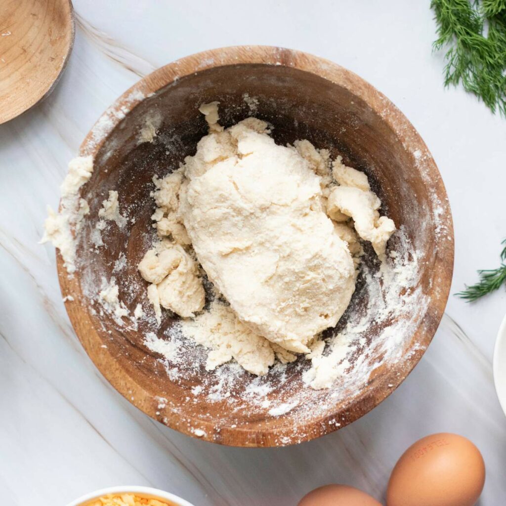 A wooden bowl containing a mound of dough sits on a marble surface.