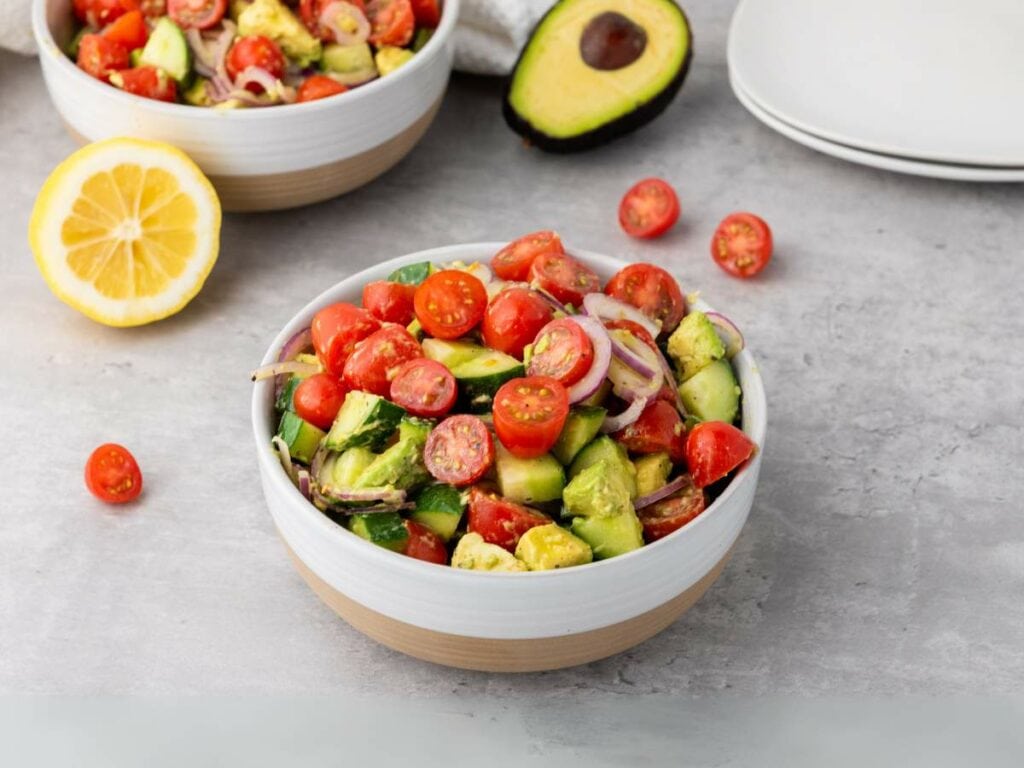 A bowl of summer salad with cherry tomatoes, avocado, red onion, and greens.