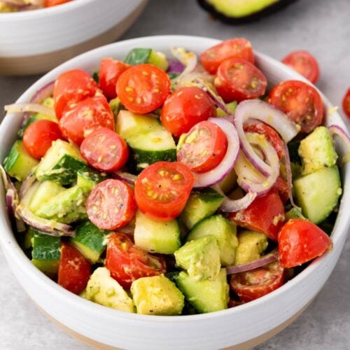 A bowl of ssummer salad containing cherry tomatoes, avocado, cucumber, and red onion.