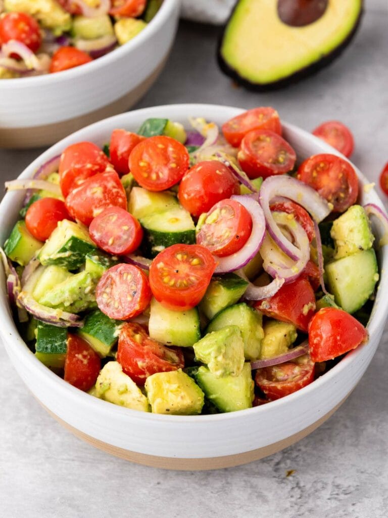 A bowl of ssummer salad containing cherry tomatoes, avocado, cucumber, and red onion.