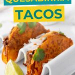 Two quesabirria tacos with shredded meat, onions, and cilantro are served in a white taco holder with a lime wedge on the side.