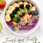 A berry smoothie bowl topped with sliced banana, kiwi, blueberries, strawberries, and sunflower seeds on a white surface.