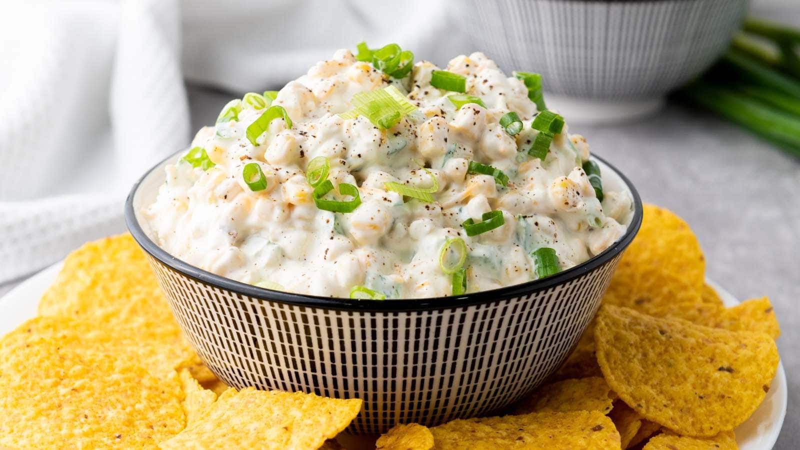 A creamy corn dip topped with chopped green onions, surrounded by tortilla chips.