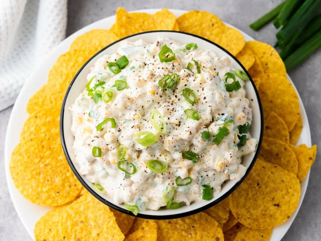 A bowl of creamy corn dip topped with chopped green onions.
