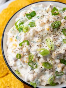 Close-up of a creamy corn dip garnished with sliced green onions and black pepper.