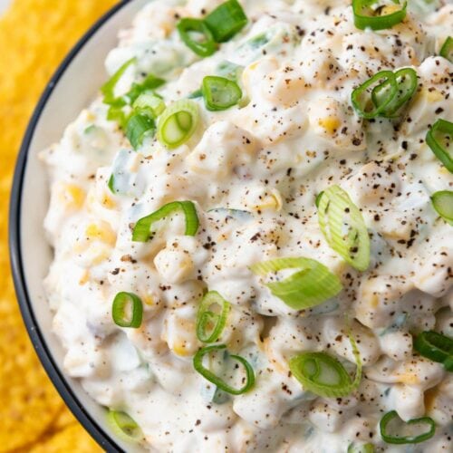 Close-up of a creamy corn dip garnished with sliced green onions and black pepper.