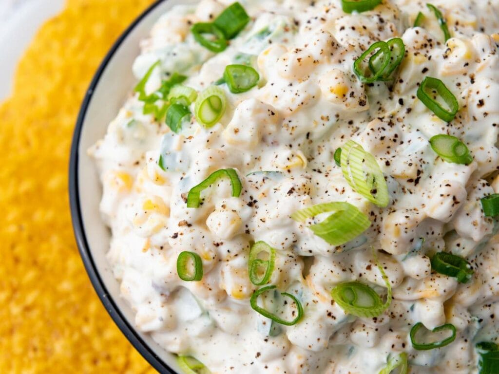 A close-up of a creamy corn dip with chopped green onions.