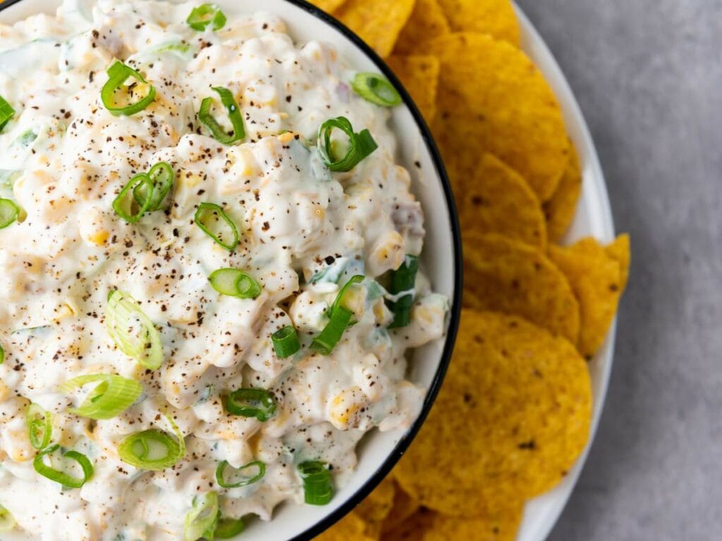 A bowl of creamy corn dip garnished with sliced green onions.