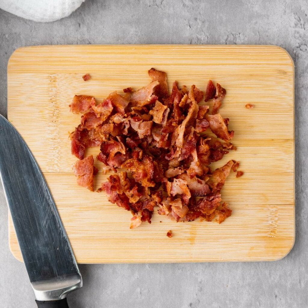 Chopped cooked bacon on a wooden cutting board .