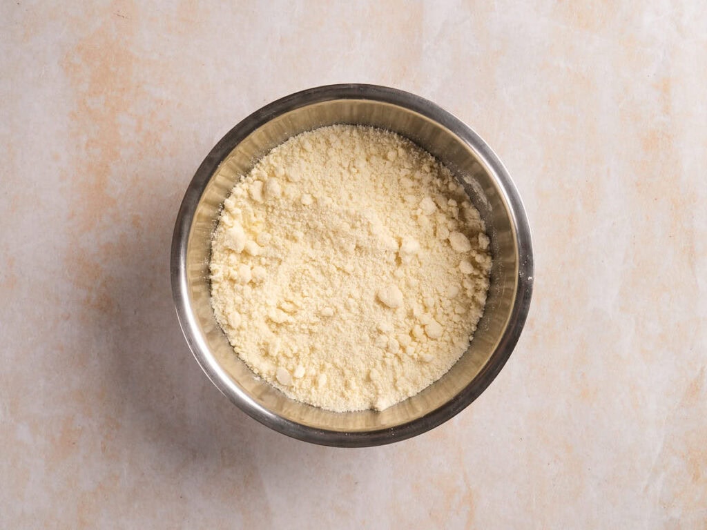 A metal bowl filled with finely ground yellowish powder, placed on a light-colored textured surface.