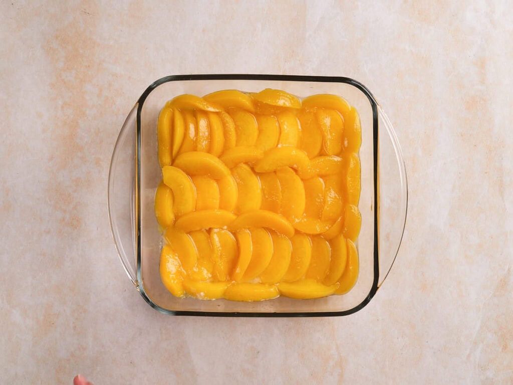 A glass baking dish filled with neatly arranged sliced peaches on a light-colored surface.