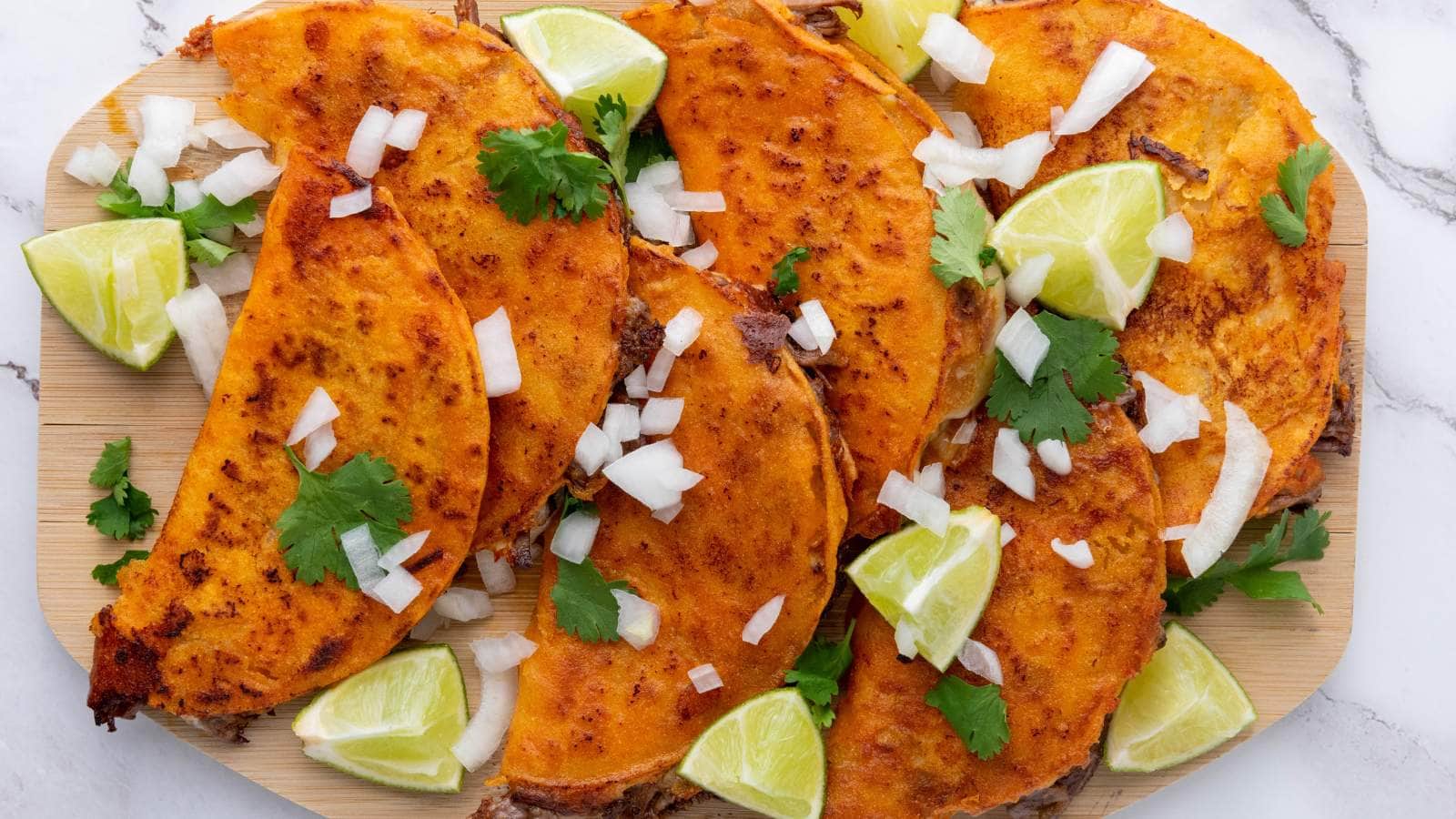 A quesabirria tacos topped with chopped onions, cilantro, and lime wedge.