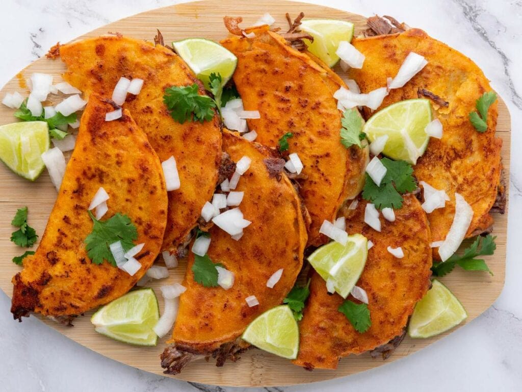 A quesabirria tacos garnished with chopped onions, cilantro, and lime wedges.